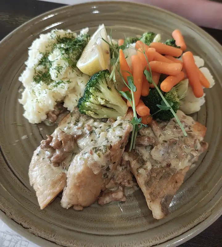 Ryba z puree ziemniaczanym, marchewką i brokułami na talerzu w restauracji Łóżko
